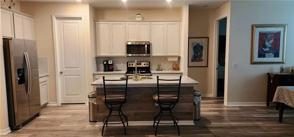 Kitchen featuring appliances with stainless steel finishes, a breakfast bar area, light stone countertops, an island with sink, and white cabinets