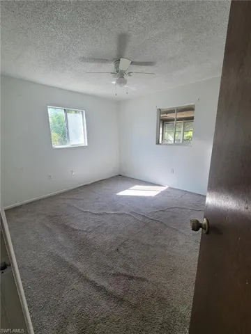 Carpeted spare room with ceiling fan, healthy amount of natural light, and a textured ceiling