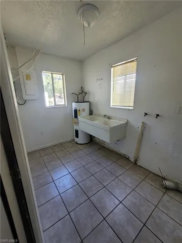Full bath with light tile patterned flooring, electric water heater, a textured ceiling, and electric panel