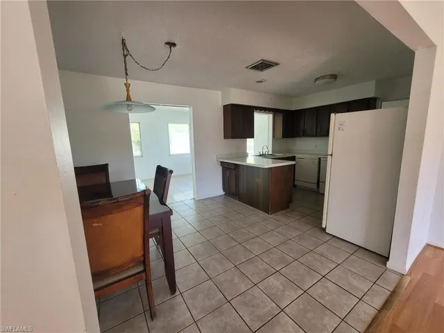 Kitchen featuring light countertops, white appliances, a peninsula, light tile patterned floors, and decorative light fixtures