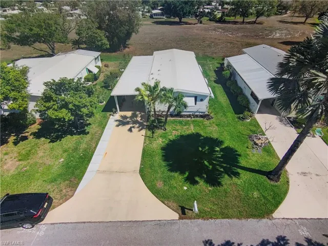 Property featuring a long driveway, attached carport, mature palm trees, and a spacious green lawn