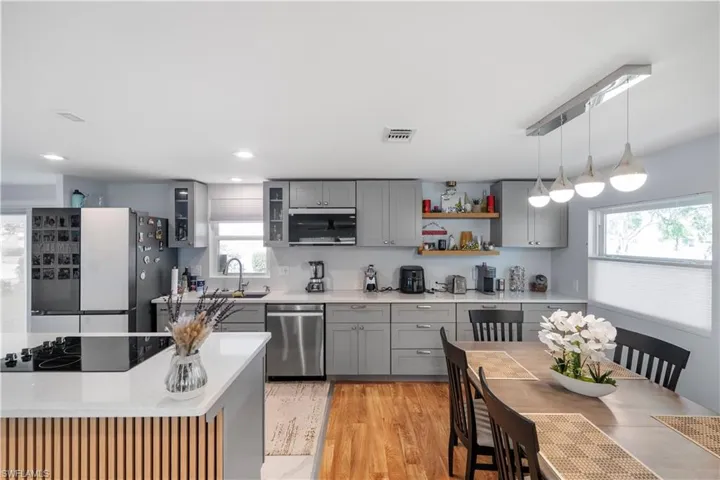 Open-concept kitchen featuring gray shaker-style cabinetry, stainless steel appliances, quartz countertops, and wood-finish flooring