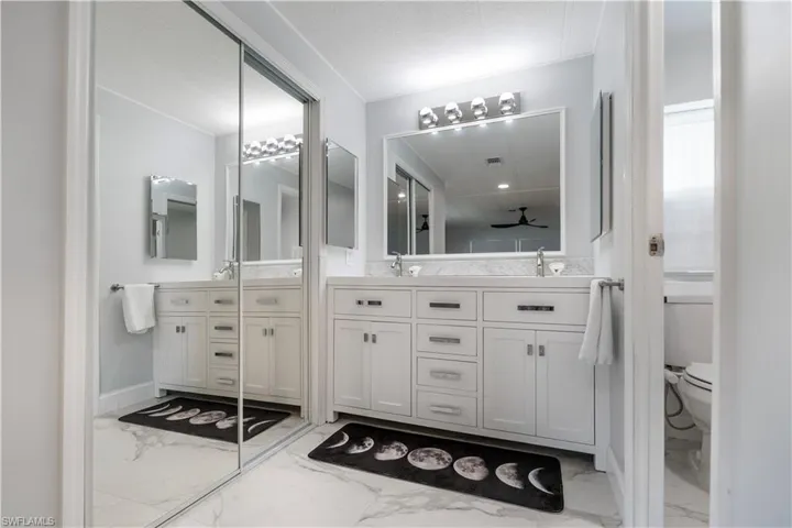 Bathroom featuring dual vanities with white cabinetry, light-toned countertops, and framed mirrors