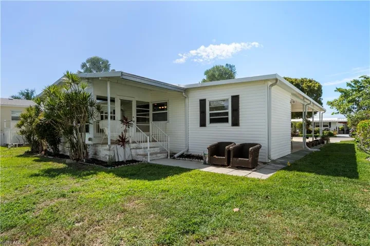 White siding exterior featuring a covered porch with railings, a paved patio area, and a covered carport
