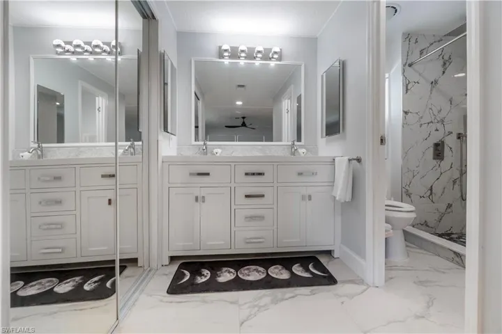 Double vanity featuring white cabinetry with silver hardware, white countertops, and dual mirrors with integrated lighting