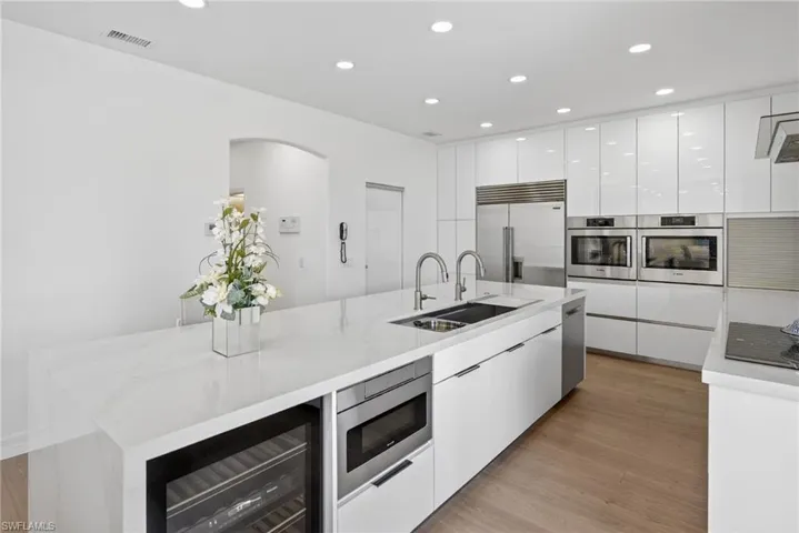 Kitchen with white cabinetry, modern cabinets, light stone countertops, beverage cooler, and recessed lighting