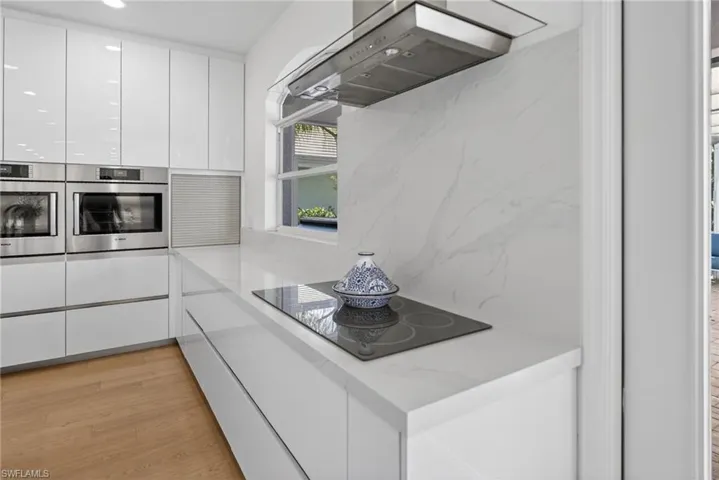 Kitchen featuring modern cabinets, white cabinets, ventilation hood, stainless steel double oven, and light wood-style floors