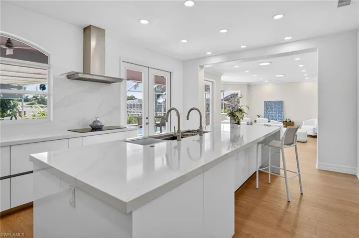 Kitchen with white cabinets, light wood-style floors, backsplash, light stone counters, and recessed lighting