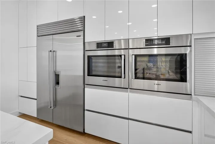 Kitchen featuring modern cabinets, stainless steel appliances, white cabinets, and light wood-style floors