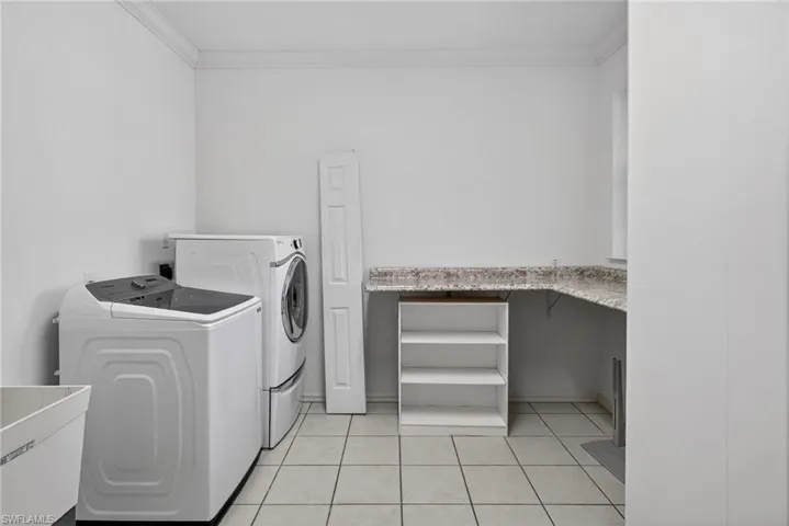 Laundry area with ornamental molding, washing machine and dryer, and light tile patterned flooring