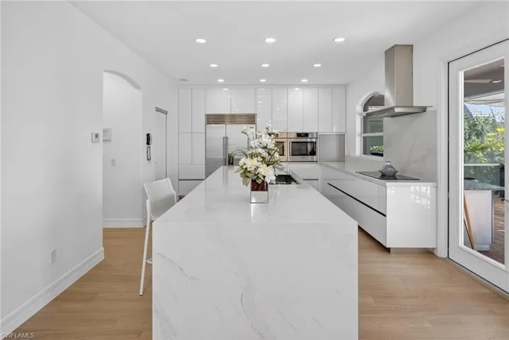 Kitchen with white cabinets, modern cabinets, light wood-type flooring, light stone countertops, and ventilation hood