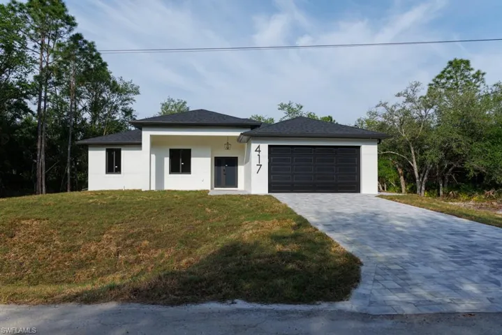 View of front of property featuring a front yard, decorative driveway, stucco siding, and an attached garage