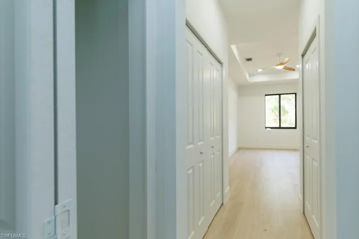 Hallway with baseboards, a tray ceiling, visible vents, and light wood-type flooring
