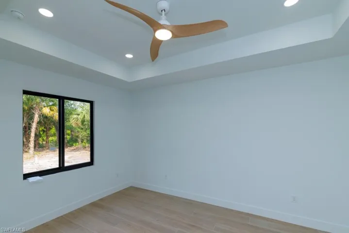 Spare room with light wood-style flooring, baseboards, recessed lighting, a ceiling fan, and a raised ceiling