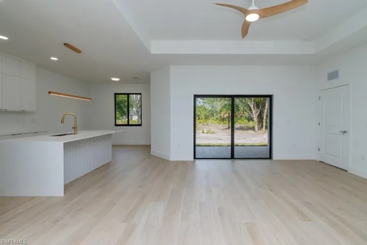 Unfurnished living room featuring a sink, a ceiling fan, light wood-style flooring, baseboards, and visible vents