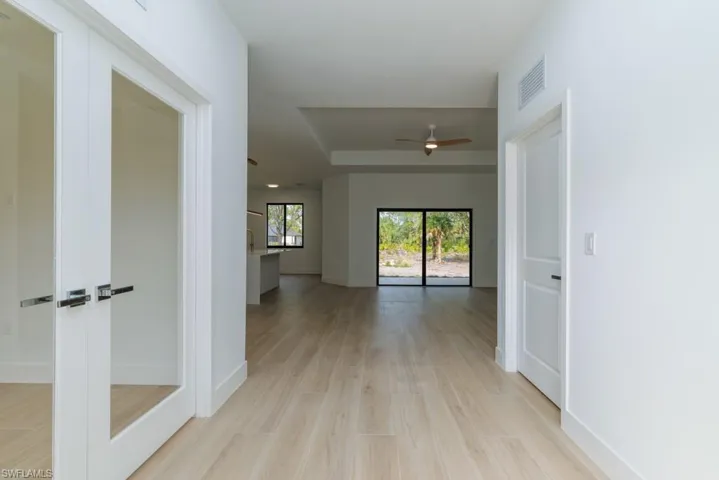 Corridor with baseboards, visible vents, light wood-style floors, and a raised ceiling