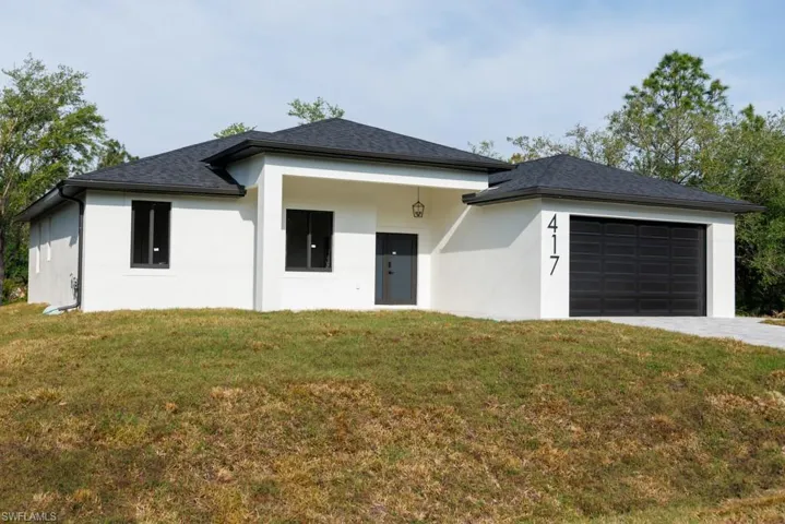 Prairie-style home with stucco siding, driveway, a garage, and a front lawn