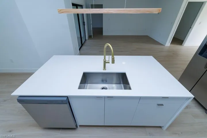 Kitchen with an island with sink, light countertops, a sink, dishwasher, and baseboards