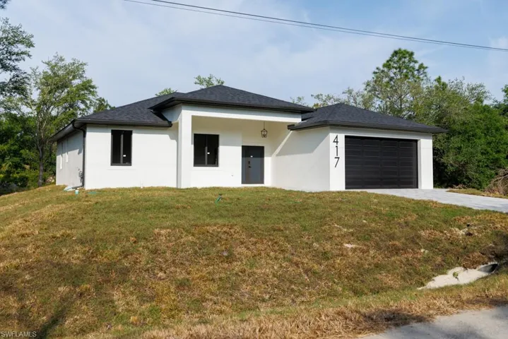 View of front of property featuring a front lawn, driveway, stucco siding, and a garage