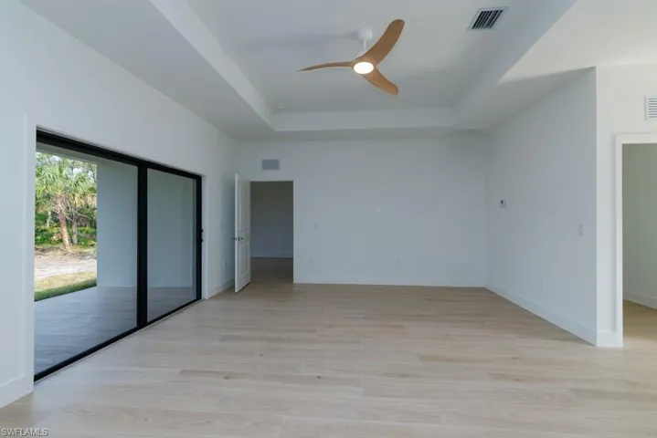Unfurnished bedroom with baseboards, light wood-style flooring, a tray ceiling, and visible vents