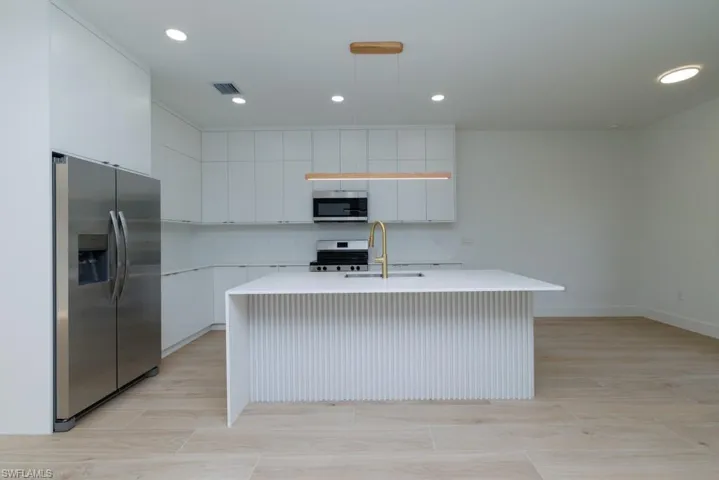 Kitchen featuring a center island with sink, light countertops, a sink, and stainless steel appliances