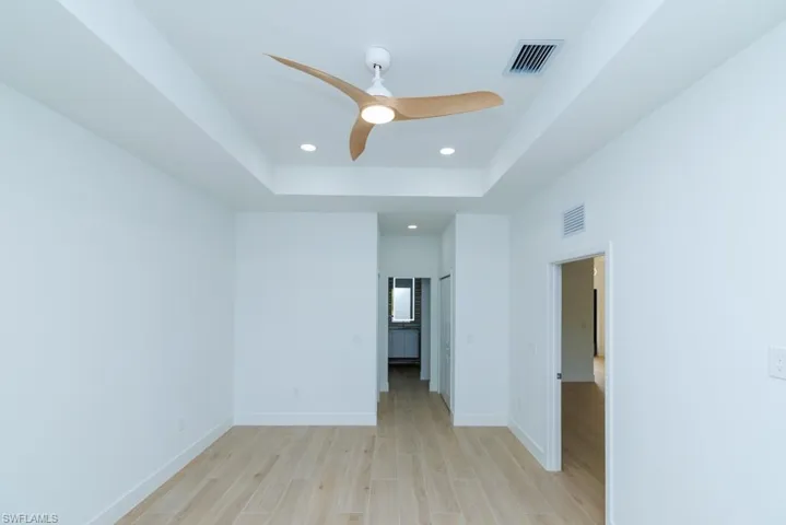 Spare room with baseboards, visible vents, light wood-style floors, and a raised ceiling