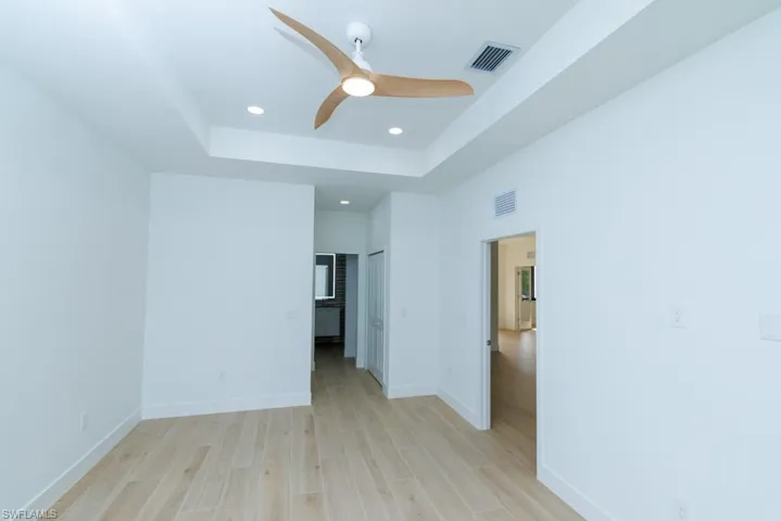 Unfurnished bedroom with baseboards, a tray ceiling, visible vents, and light wood-style floors