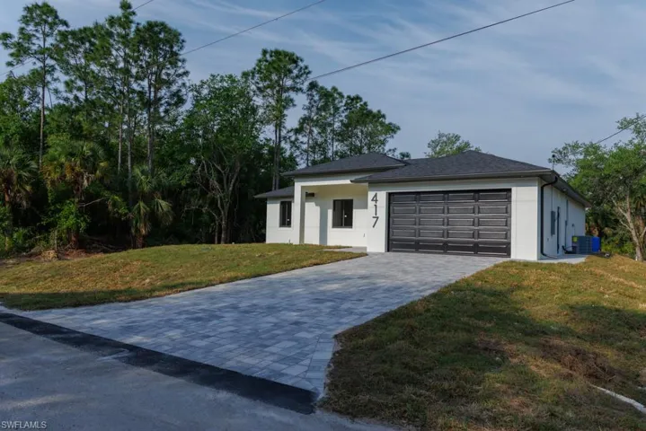 View of front facade with central AC unit, decorative driveway, a garage, a front lawn, and stucco siding