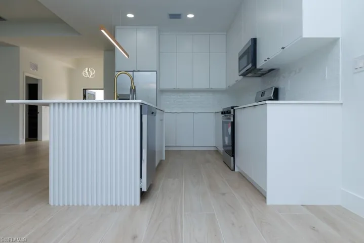 Kitchen featuring decorative backsplash, modern cabinets, stainless steel range with electric cooktop, and visible vents