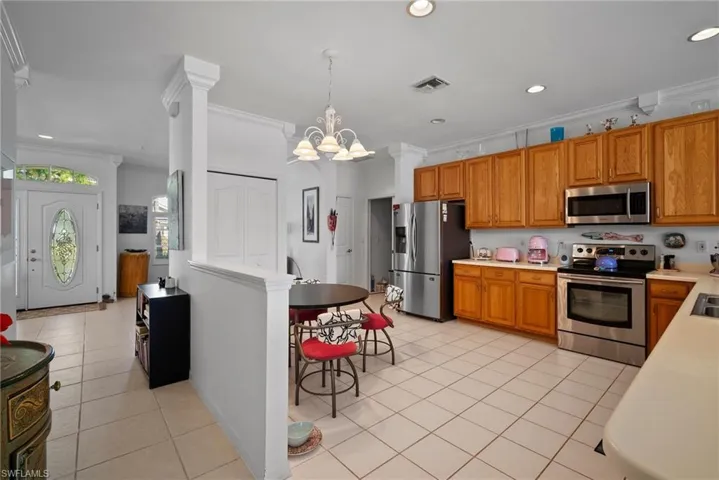 Kitchen with light tile patterned flooring, appliances with stainless steel finishes, decorative light fixtures, ornamental molding, and a notable chandelier
