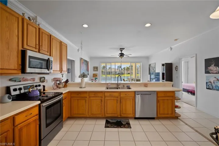 Kitchen featuring sink, light tile patterned floors, stainless steel appliances, ornamental molding, and kitchen peninsula