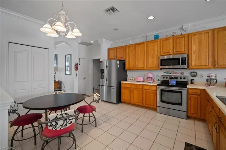 Kitchen with crown molding, decorative light fixtures, light tile patterned floors, a notable chandelier, and stainless steel appliances
