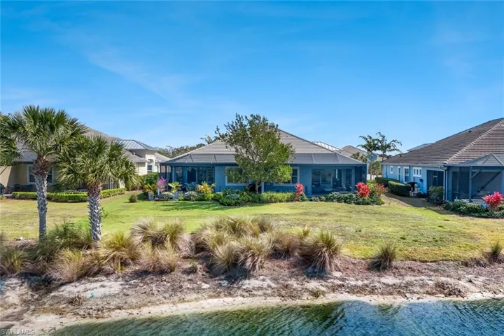 Rear view of property featuring a sunroom, a lawn, a water view, and glass enclosure