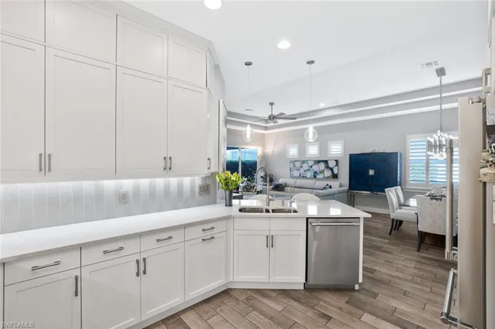 Kitchen with open floor plan, ceiling fan, white cabinets, stainless steel appliances, and light stone counters