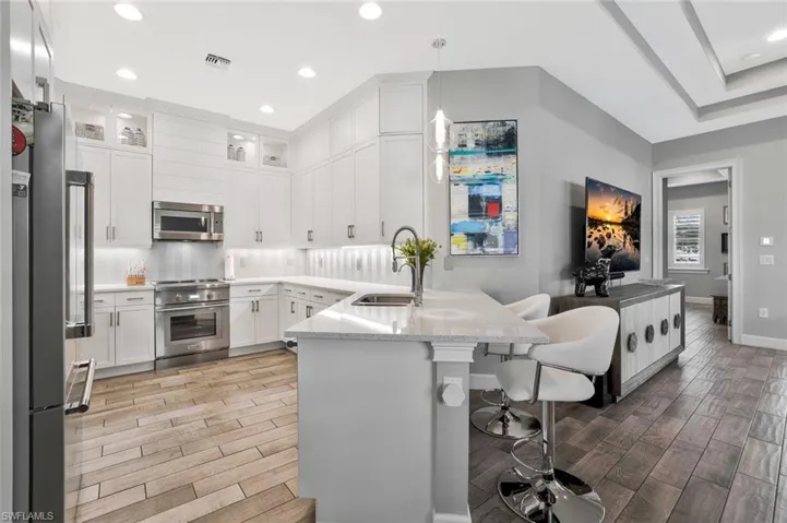Kitchen with a peninsula, a kitchen breakfast bar, tasteful backsplash, white cabinets, and wood tiled floors
