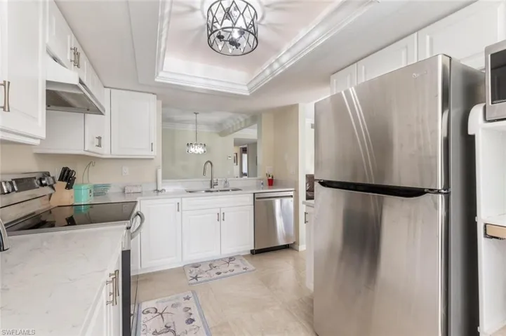 Kitchen with appliances with stainless steel finishes, a tray ceiling, sink, decorative light fixtures, and white cabinetry