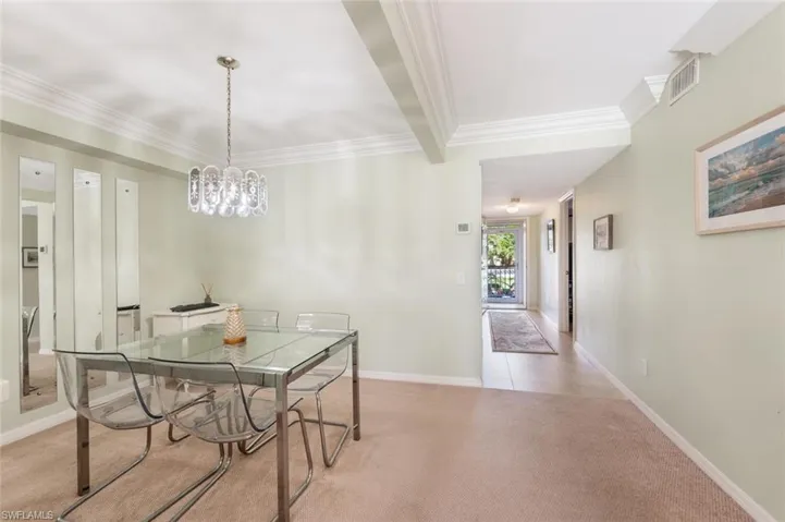 Dining space with beamed ceiling, light colored carpet, and ornamental molding