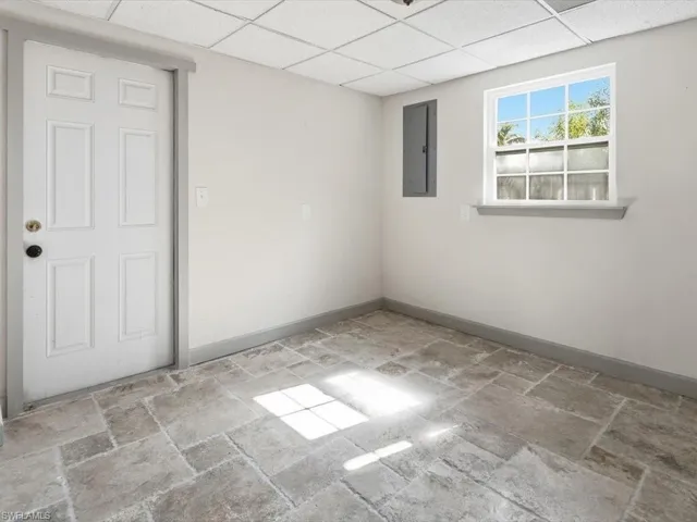 Empty room featuring a drop ceiling, electric panel, and stone tile floors
