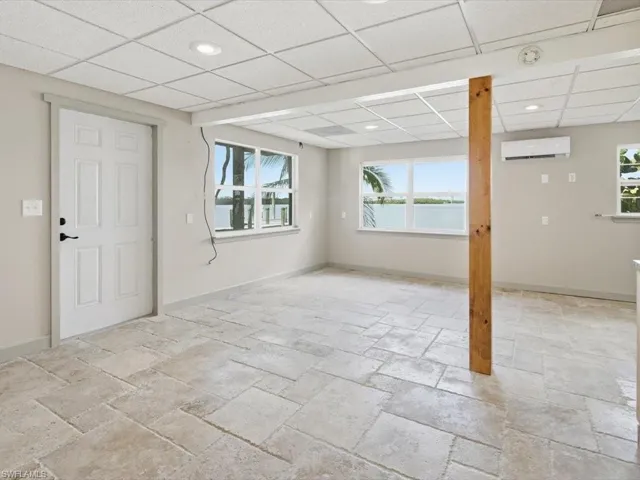 Below grade area featuring a drop ceiling, stone tile floors, recessed lighting, and an AC wall unit
