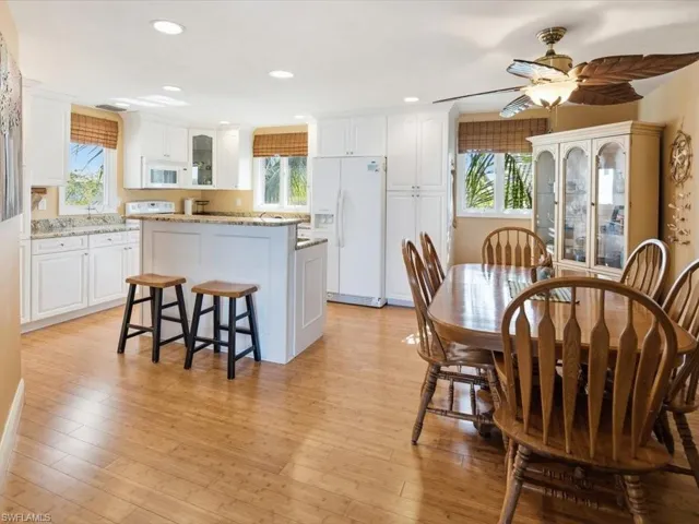 Kitchen with a breakfast bar, glass insert cabinets, white cabinets, white appliances, and recessed lighting
