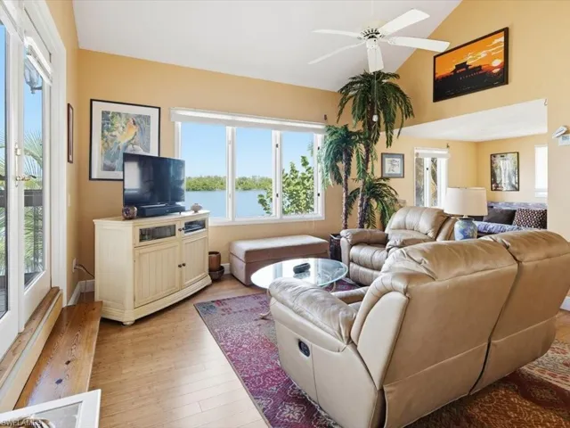Living room featuring healthy amount of natural light, light wood-type flooring, a ceiling fan, and lofted ceiling