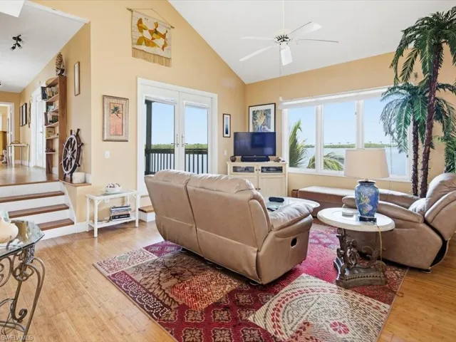 Living area with healthy amount of natural light, light wood finished floors, high vaulted ceiling, a ceiling fan, and french doors