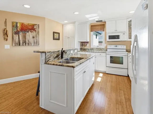 Kitchen with white appliances, white cabinetry, light stone counters, a center island with sink, and light wood-style floors