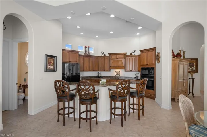 Kitchen with arched walkways, a breakfast bar area, dark stone countertops, a kitchen island with sink, and a high ceiling