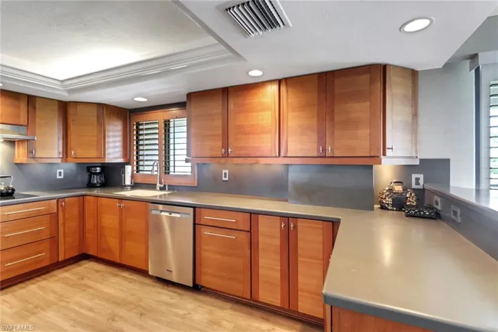 Kitchen with stainless steel dishwasher, a sink, recessed lighting, brown cabinetry, and light wood finished floors