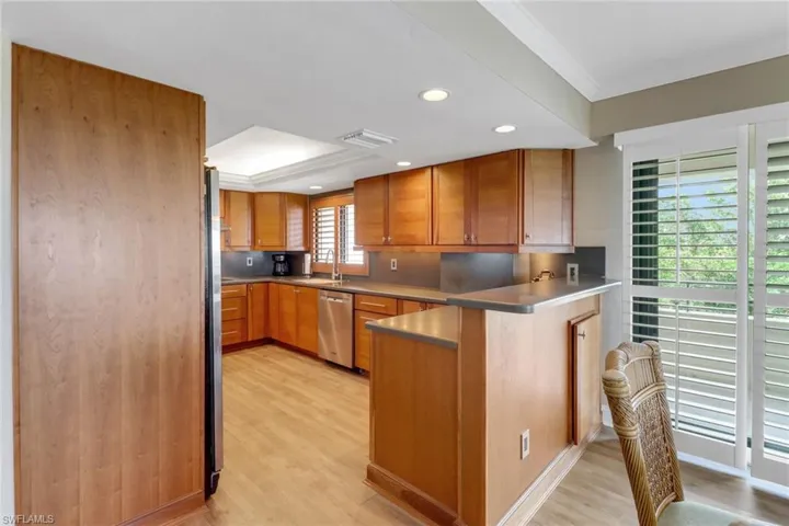 Kitchen with appliances with stainless steel finishes, a peninsula, light wood-type flooring, ornamental molding, and brown cabinets