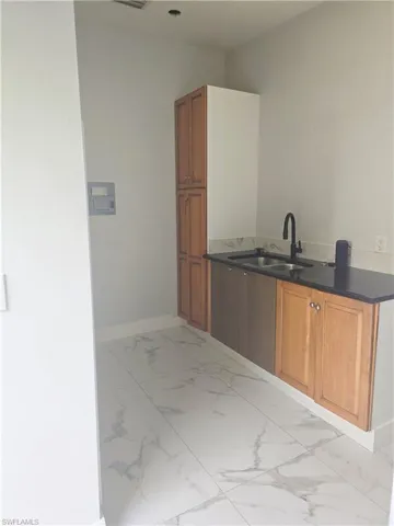 Mother-in-law Kitchen featuring brown cabinetry, light marble finish flooring, and dark stone counters