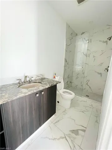 Bathroom featuring vanity, a marble finish shower, and light marble finish floors