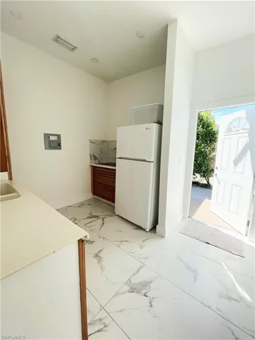 Kitchen with wood finish cabinetry, freestanding refrigerator, light countertops, and light marble finish flooring