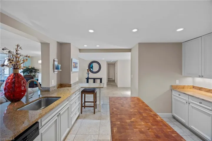 Kitchen featuring wooden counters, a breakfast bar, dishwashing machine, sink, and white cabinets